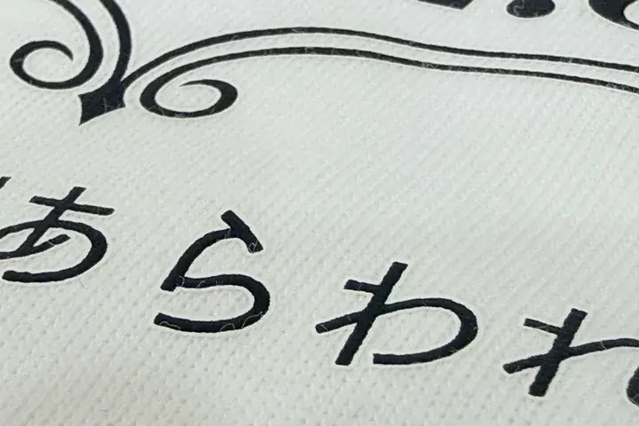 フルカラー転写(DTF)プリントの拡大写真。白いボディに黒い文字を転写し、文字の周りにボディと同色(白)のフチ(塗り足し)がついている